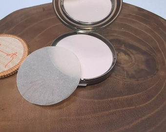 May include: A silver compact with a mirror and a white powder puff. The compact is open and the powder puff is sitting on top of the powder.