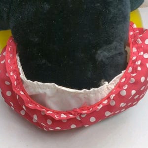 May include: A close-up of a plush toy featuring a black head and a red polka-dot bow. The bow is red with white polka dots and has a white lining. The toy is likely a character from a popular cartoon.