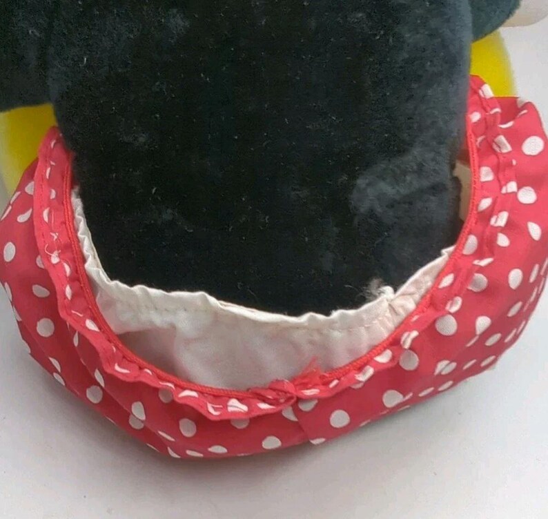 May include: A close-up of a plush toy featuring a black head and a red polka-dot bow. The bow is red with white polka dots and has a white lining. The toy is likely a character from a popular cartoon.