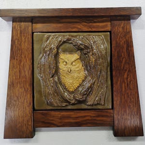 May include: A ceramic tile with a raised image of an owl in a tree, framed in a dark wood frame.