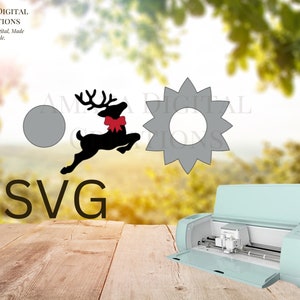 Könnte beinhalten: Eine digitale Schneidemaschine mit hellblauer Außenhülle und offenem Deckel. Die Maschine steht auf einer Holzoberfläche. Auf der Oberfläche befinden sich drei SVG-Ausschnitte: ein Kreis, ein Stern und ein Rentier mit einer roten Schleife.