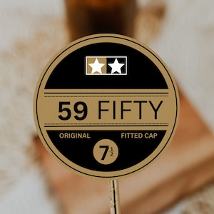 Puede incluir: Una pegatina circular marrón y negra con el texto "59 FIFTY" en blanco. La pegatina también presenta dos estrellas blancas sobre un fondo negro y el texto "ORIGINAL" y "FITTED CAP" en blanco. La pegatina tiene un número negro "7 1/2" en el centro.