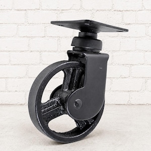 May include: A black metal swivel castor wheel featuring a spoked design and a flat square mounting plate with four pre-drilled holes. The industrial-style component has a matte finish and a sturdy bracket that connects the wheel to the top plate.