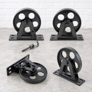 Puede incluir: Cuatro poleas de metal negro con placas de montaje. Cada polea presenta una rueda circular con cinco radios y un soporte triangular. Una polea incluye una cadena de metal corta con un perno roscado unido a la placa de montaje.