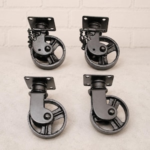 May include: A set of four black metal swivel castors, each featuring a square mounting plate with four screw holes, a sturdy wheel with spokes, and a locking mechanism attached by a small chain on two of the units for secure positioning.