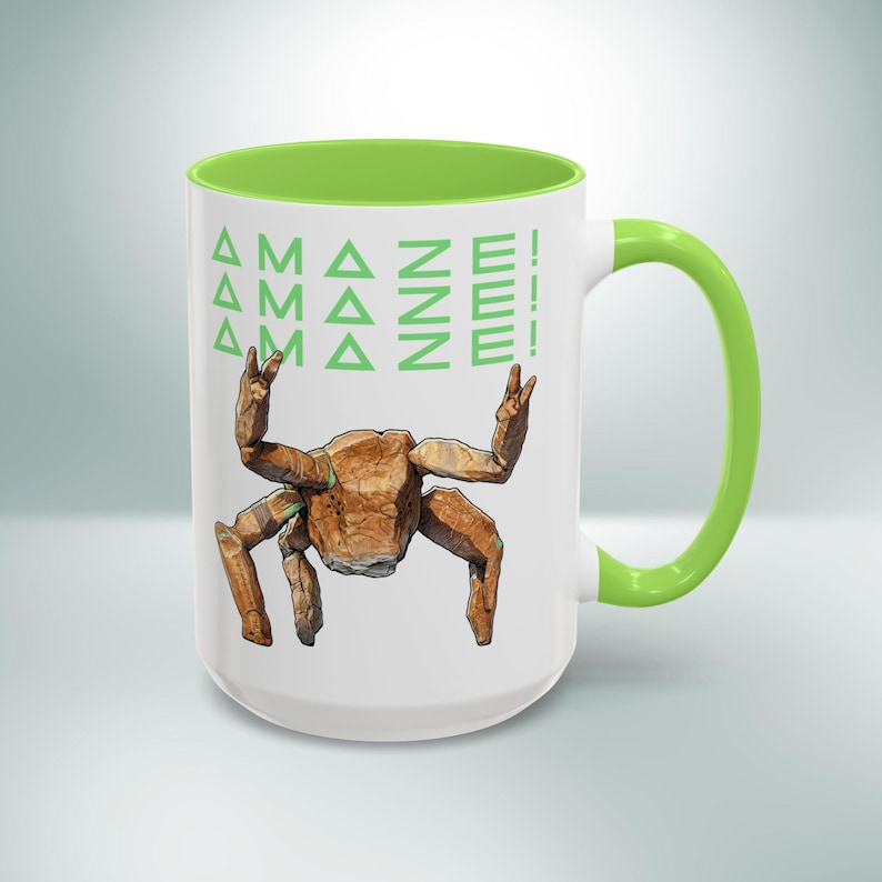 Puede incluir: Taza de cer&aacute;mica blanca con interior, asa y borde verdes. La taza presenta una ilustraci&oacute;n de cangrejo geom&eacute;trico marr&oacute;n y el texto "AMAZE!" en verde. Una taza de caf&eacute; divertida y &uacute;nica.