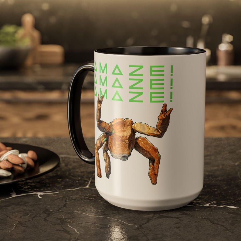 Puede incluir: Una taza de caf&eacute; blanca grande con asa e interior negros. La taza presenta una ilustraci&oacute;n de cangrejo estilizada marr&oacute;n con el texto "AMAZE!" en verde. La taza est&aacute; sobre una encimera oscura.