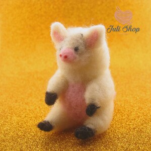 May include: A handmade, off-white felt piglet figurine with pink inner ears, snout, and belly. The piglet has black hooves and is sitting upright. The text "Juli Shop" is in the upper right corner.