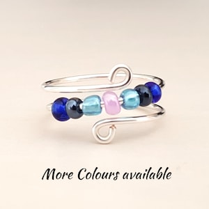 Puede incluir: Un anillo de plata con un diseño de cuentas. Las cuentas son azules, verde azulado, rosas y negras. El anillo es ajustable y tiene un diseño simple y elegante.