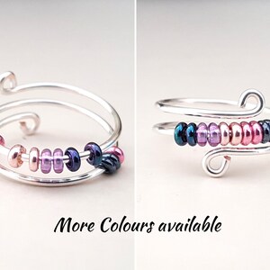 Puede incluir: Un anillo de plata con una banda doble y una fila de cuentas de colores. Las cuentas son de color rosa, morado y negro. Hay más colores disponibles.