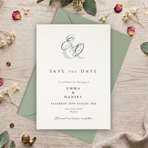 May include: A white rectangular save the date card featuring a large grey ampersand and black script initials E and D. The text reads Save the Date to celebrate the marriage of Emma and Daniel on Saturday 26th August 2028 at Lake View Hotel Walton.