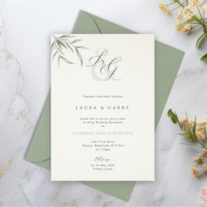 May include: A cream-coloured wedding reception invitation card featuring the initials L and G in a decorative script font, green leaf illustrations, and black text detailing the event for Laura and Garry on Saturday 26th August 2028.