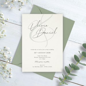May include: A cream-coloured wedding invitation card with black text featuring the names Olivia and Daniel in a large script font, placed on a sage green envelope. The text includes the date 26th August 2028 and venue details for the event.