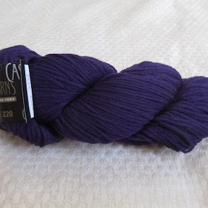 May include: A skein of deep purple yarn with a black label that reads "Cascade Yarns" and "220". The yarn is tightly wound and has a soft, textured appearance, perfect for knitting or crocheting projects.