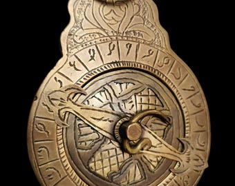 May include: A brass sundial with Arabic numerals and intricate engravings. The sundial has a movable arm with a decorative design.