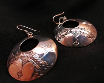 May include: A pair of silver earrings with a circular design. The earrings feature a detailed, intricate pattern and a smooth, polished finish.