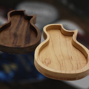 May include: Three wooden guitar-shaped trinket dishes. One is made of light wood, one is made of dark wood, and one is made of a lighter wood with a more pronounced grain.
