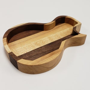 Peut inclure: Un plateau en bois en forme de guitare, fait de plusieurs types de bois, avec une finition naturelle.