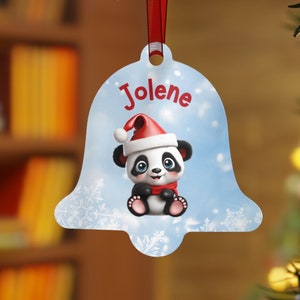 Op de afbeelding: Een klokvormige kerstversiering met een cartoon panda met een kerstmuts en sjaal. De naam "Jolene" staat in rode letters. Opgehangen aan een rood lint.