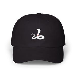 May include: Black baseball cap with a white snake emblem and a red heart detail. The cap has a curved peak and a structured crown. The snake design is embroidered on the front, suitable for casual wear.