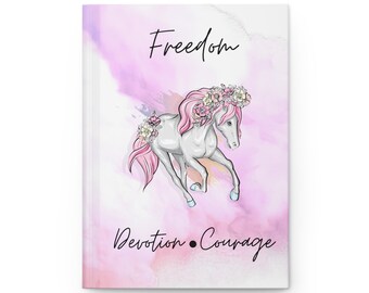 May include: A hardcover journal with a white cover featuring a watercolor background of pink and purple hues. A white unicorn with a pink mane and floral crown is illustrated on the cover. The words "Freedom", "Devotion", and "Courage" are written in black script.