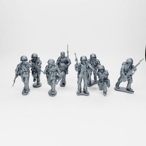 Puede incluir: Un grupo de soldados de juguete de plástico gris en varias poses, incluyendo de pie, arrodillados y corriendo. Cada figura está equipada con un casco y un arma, como un rifle o una ametralladora. Sobre un fondo blanco.
