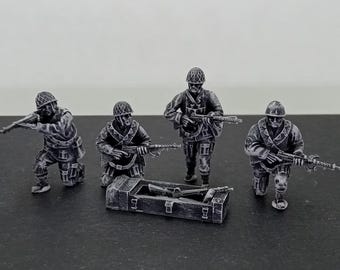Könnte beinhalten: Miniatur-Soldaten in verschiedenen Posen, kniend und stehend, mit Gewehren. In der Mitte befindet sich eine kleine graue Kiste mit Waffen. Die Figuren sind detailliert und scheinen Teil eines militärischen Dioramas oder Modells zu sein.