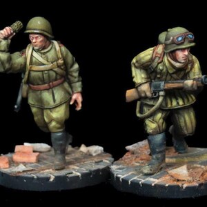 May include: Two painted miniature figures of World War II Soviet soldiers. One soldier is holding a grenade and the other is holding a rifle. Both figures are wearing military uniforms and helmets.