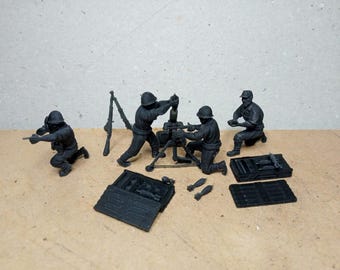 Könnte beinhalten: Ein schwarzes Miniatur-Militärdiorama mit Soldaten, die einen Mörser bedienen. Die Szene umfasst Soldaten in verschiedenen Posen, einen Mörser, Munitionskisten und zusätzliche Waffen. Die Figuren sind detailliert.