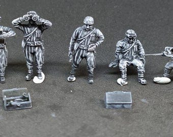 Könnte beinhalten: Graue Miniaturfiguren von Soldaten in verschiedenen Posen, darunter eine mit einem Fernglas und eine kniende. Zwei kleine graue Koffer sind ebenfalls vorhanden. Die Figuren sind detailliert und scheinen Teil eines Modellbausatzes zu sein.