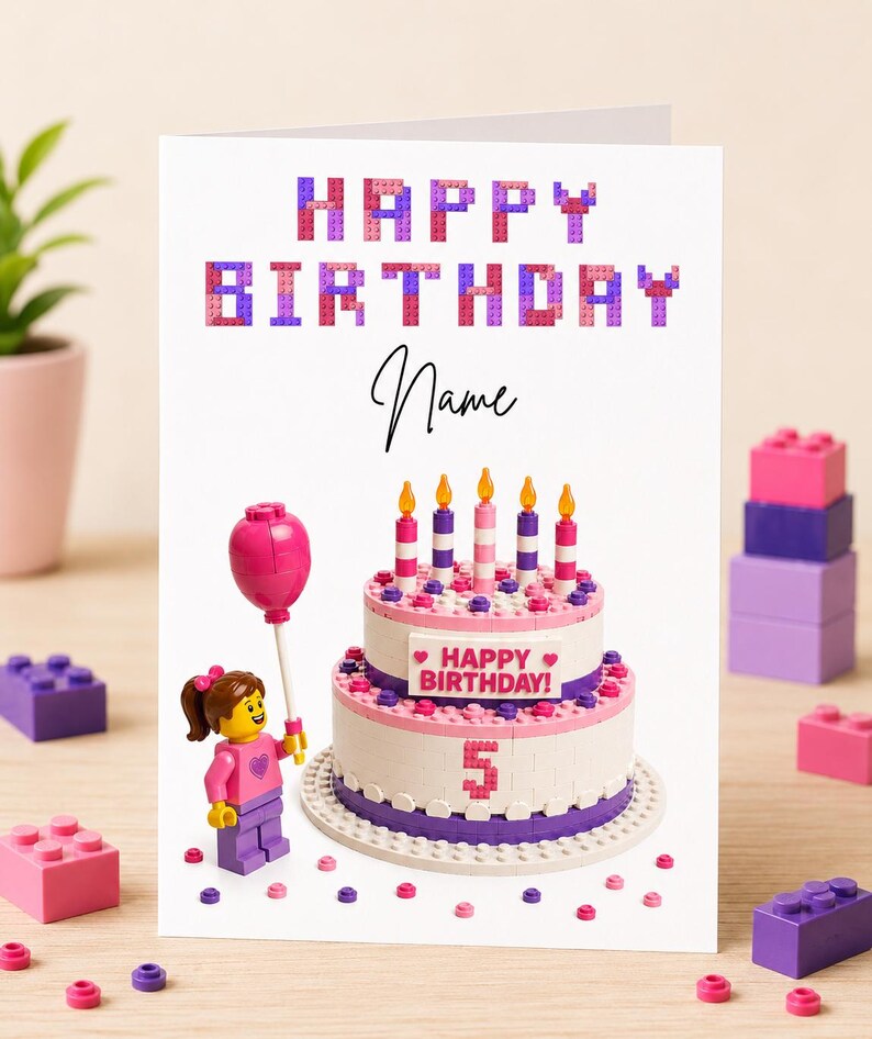 May include: A birthday card with a Lego-themed design. The card features the words "HAPPY BIRTHDAY" in block letters, a cake with candles, and a Lego figure holding a balloon. The number "5" is displayed on the cake.