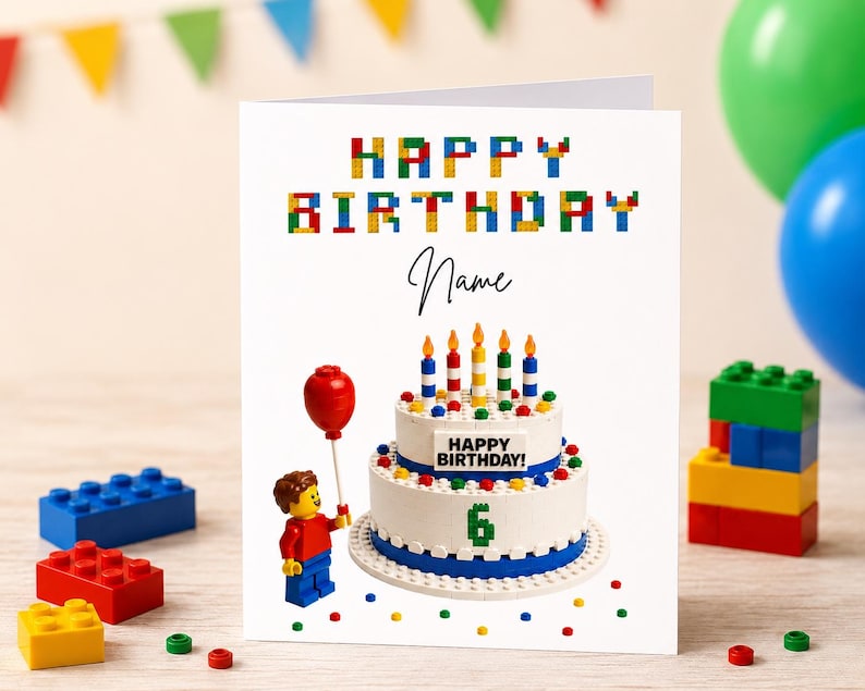 May include: A birthday card with a Lego-themed design. The card features the words "HAPPY BIRTHDAY" in colourful block letters. A cake with candles and the number 6 is on the card. A Lego figure holds a red balloon.