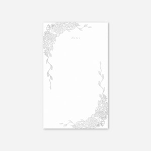 May include: A white notepad with a floral border design. The border features detailed line art of roses and leaves in a soft gray color. The word "Notes" is printed in a delicate font at the top.