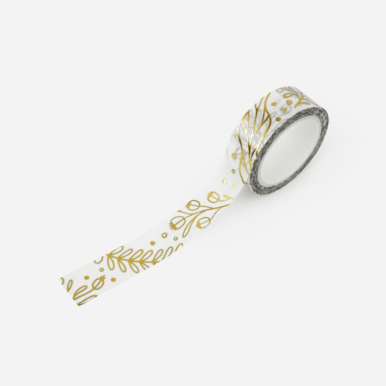May include: White washi tape with a gold floral pattern. The tape is rolled up and partially unrolled, showing the design.
