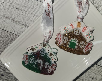 Peut inclure: Deux décorations de maison en pain d'épices avec du glaçage blanc, des cannes en sucre rouge et des paillettes. L'une est verte et l'autre est brune.