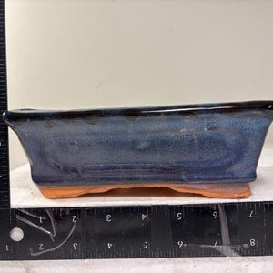 May include: A rectangular bonsai pot with a blue glazed finish and a brown base. The pot is approximately 8 inches long and 4 inches wide. The pot has a glossy finish and is suitable for bonsai trees.