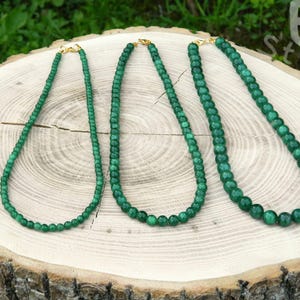 May include: Three green jade necklaces of varying lengths, made of round beads, on a wooden surface.