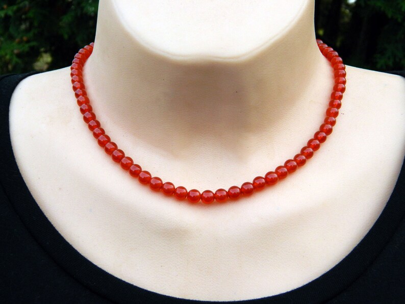 May include: A necklace of small, round, faceted red beads. The necklace is displayed on a mannequin, showcasing the jewelry's design and color. The beads are a vibrant shade of red.