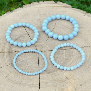 Peut inclure: Quatre bracelets en pierres précieuses bleu clair de tailles différentes sur une surface en bois.
