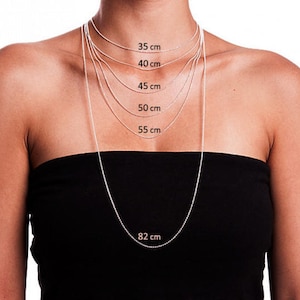 May include: Silver chain necklaces of various lengths, displayed on a person. The lengths are labeled in centimeters: 35 cm, 40 cm, 45 cm, 50 cm, 55 cm, and 82 cm. The necklaces are shown against a black strapless top.