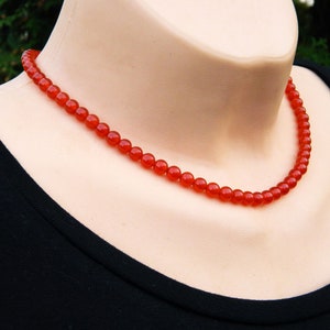 May include: A vibrant red beaded necklace. The necklace is composed of small, round beads, creating a continuous strand. The beads are a rich, saturated red color, and the necklace is displayed on a mannequin.