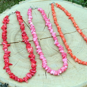 Puede incluir: Tres collares de coral de diferentes tonos de rosa y rojo, colocados sobre una superficie de madera.