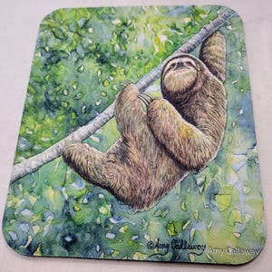 May include: Watercolor painting of a brown sloth hanging upside down from a branch in a green leafy tree. The sloth has a relaxed expression and is surrounded by green leaves. The painting is signed "Amy Callaway" in the bottom right corner.