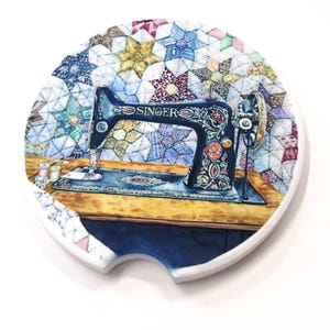 Könnte beinhalten: Runder Auto-Untersetzer mit einer Illustration einer Vintage Singer Nähmaschine. Die schwarze Maschine ist mit floralen Akzenten und dem Wort "SINGER" versehen. Der Hintergrund zeigt ein farbenfrohes Steppmuster mit weißem Rand.