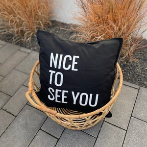 Könnte beinhalten: Schwarzes Kissen mit weißem Text "Nice to see you" in einem geflochtenen Korb.