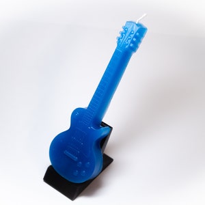 May include: A blue electric guitar shaped candle on a black stand.