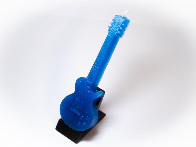 May include: A blue electric guitar shaped candle on a black stand.