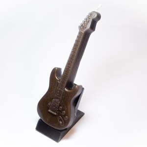 May include: A brown electric guitar shaped candle on a black stand.