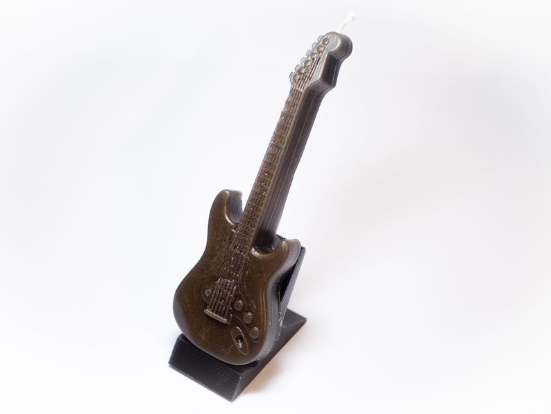 May include: A brown electric guitar shaped candle on a black stand.