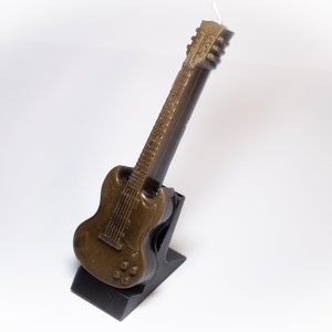 May include: A brown guitar-shaped candle on a black stand. The candle is detailed with a textured finish and a black pickguard.